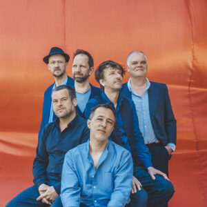 Photo des 6 membres du groupe de Debout Sur Le Zinc, fixant l'objectif. Avec en fond, un drap satiné orange3