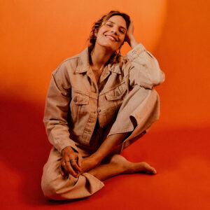 photo de l'artiste Vanille, assise par terre, sur fond orange.
