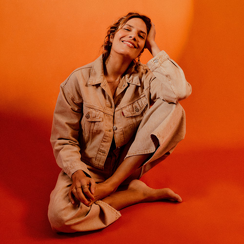photo de l'artiste Vanille, assise par terre, sur fond orange.